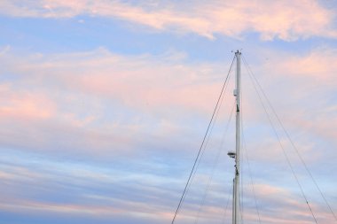 Yelkenli bir yatın direğinin alçak açılı görüntüsü. Yumuşak güneş ışığı, parlayan günbatımı gökyüzü. Ulaşım, eğlence, eğlence, gezi, spor, yelkencilik, yarış, yat