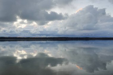 Forest river (lake) at sunset. Dramatic sky, dark glowing clouds. Symmetry reflections in a crystal clear water. Panoramic autumn landscape. Nature, environment, ecology, weather, climate change