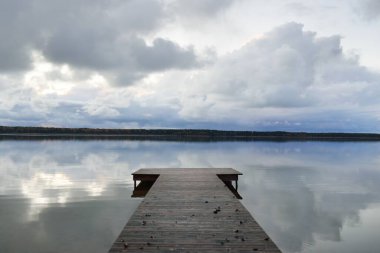 Gün batımında Orman Nehri (Lake). Ahşap iskele. Dramatik gökyüzü, karanlık, parlak bulutlar. Kristal berrak suda simetri yansımaları. Panoramik sonbahar manzarası. Doğa, ekoloji, ekoloji, ekolojik tatil beldesi