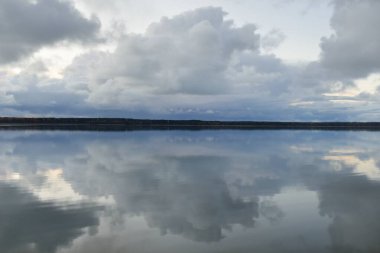 Gün batımında Orman Nehri (Lake). Dramatik gökyüzü, karanlık, parlak bulutlar. Kristal berrak suda simetri yansımaları. Panoramik sonbahar manzarası. Doğa, çevre, ekoloji, hava durumu, iklim değişikliği