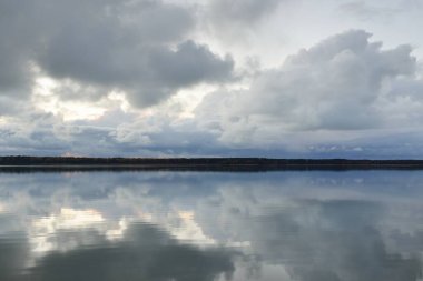 Gün batımında Orman Nehri (Lake). Dramatik gökyüzü, karanlık, parlak bulutlar. Kristal berrak suda simetri yansımaları. Panoramik sonbahar manzarası. Doğa, çevre, ekoloji, hava durumu, iklim değişikliği