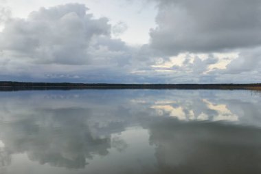 Forest river (lake) at sunset. Dramatic sky, dark glowing clouds. Symmetry reflections in a crystal clear water. Panoramic autumn landscape. Nature, environment, ecology, weather, climate change