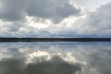 Gün batımında Orman Nehri (Lake). Dramatik gökyüzü, karanlık, parlak bulutlar. Kristal berrak suda simetri yansımaları. Panoramik sonbahar manzarası. Doğa, çevre, ekoloji, hava durumu, iklim değişikliği