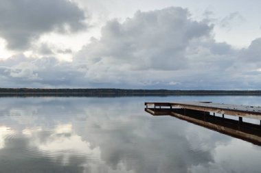 Gün batımında Orman Nehri (Lake). Ahşap iskele. Dramatik gökyüzü, karanlık, parlak bulutlar. Kristal berrak suda simetri yansımaları. Panoramik sonbahar manzarası. Doğa, ekoloji, ekoloji, ekolojik tatil beldesi