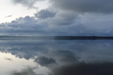 Forest river (lake) at sunset. Dramatic sky, dark glowing clouds. Symmetry reflections in a crystal clear water. Panoramic autumn landscape. Nature, environment, ecology, weather, climate change