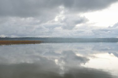 Gün batımında Orman Nehri (Lake). Dramatik gökyüzü, karanlık, parlak bulutlar. Kristal berrak suda simetri yansımaları. Panoramik sonbahar manzarası. Doğa, çevre, ekoloji, hava durumu, iklim değişikliği