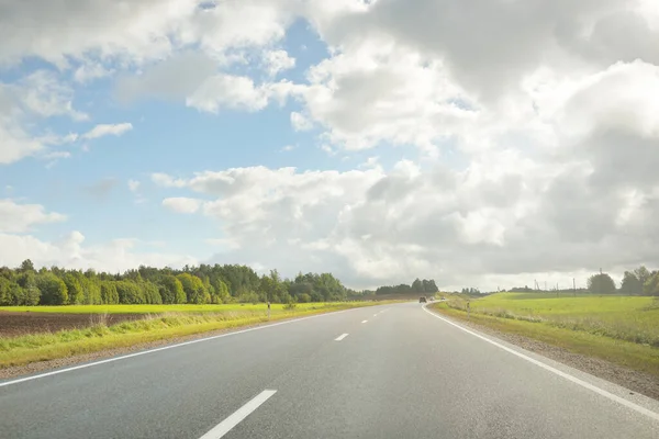 Tarlalar ve orman boyunca (asfalt yol) yol. Arabadan bak. Dramatik fırtına bulutları. Seyahat yerleri, rotalar, tatiller, lojistik, uzak yerler