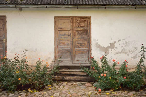 Kırsal ahşap kapılı ve pencereli geleneksel taş ev. Çiçek açan güller, güzel bahçeler. Idyllic kırsal kesim. Seyahat yerleri, yerel turizm, şehir simgeleri, bahçe düzenlemeleri, peyzaj.