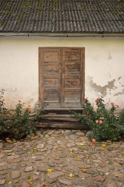 Kırsal ahşap kapılı ve pencereli geleneksel taş ev. Çiçek açan güller, güzel bahçeler. Idyllic kırsal kesim. Seyahat yerleri, yerel turizm, şehir simgeleri, bahçe düzenlemeleri, peyzaj.