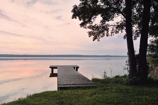 Gün batımında Orman Gölü. Ahşap iskele. Yumuşak güneş ışığı, parlayan bulutlar kristal berrak suda simetri yansımaları. Idyllic manzara. Panoramik manzara. Doğa, ekoloji, çevrecilik. Barış ve neşe kavramları