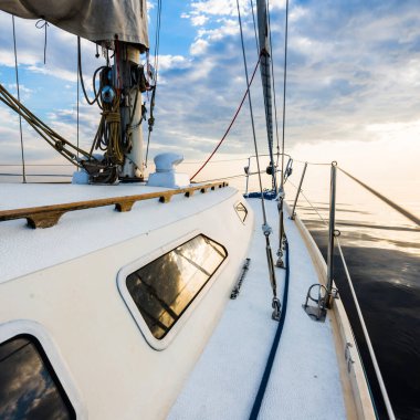 Fırtınadan sonra durgun bir suda yelken açan yelkenli bir yat. Gün batımı. Sudaki yansımalar. Baltık Denizi. Yaşam tarzı, deniz yolculuğu, yelkenli yarışı, spor, eğlence