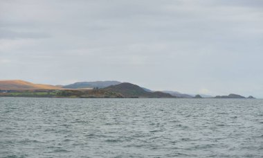 Rocky lake shore, mountain peaks, mountains, valleys and hills. Panoramic view from a sailboat. Dramatic sky. Scotland, UK. Atmospheric landscape. Travel destinations, landmarks, hiking, ecotourism