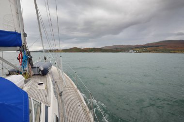 Kayalık göl kıyısında seyir halindeki ahşap meşe güvertesiyle donatılmış bir yat. İskoçya, İngiltere. Denizcilik gemisi, ulaşım, spor, eğlence aktivitesi, yelkenli yarışı, seyahat, seyahat