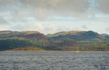 İskoçya, Rothesay 'ın kayalık kıyıları, tepeleri ve vadileri üzerinde dramatik bir gökyüzü. Yelkenliden panoramik manzara. Seyahat merkezleri, turizm, yürüyüş, dönüm noktası, ekoloji, çevre, doğa temaları