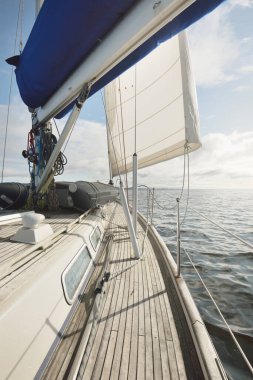 Kayalık göl kıyılarında seyir halindeki ahşap meşe güvertesiyle donatılmış modern bir yat. İskoçya, İngiltere. Güverteden pruvaya, direğe, yelkenlere bakın. Seyahat tutkusu, eğlence aktivitesi, spor, yelkenli yarışı, deniz yolculuğu.