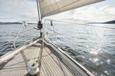 Kayalık göl kıyılarında seyir halindeki ahşap meşe güvertesiyle donatılmış modern bir yat. İskoçya, İngiltere. Güverteden pruvaya, direğe, yelkenlere bakın. Seyahat tutkusu, eğlence aktivitesi, spor, yelkenli yarışı, deniz yolculuğu.