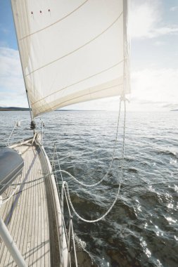 Kayalık göl kıyılarında seyir halindeki ahşap meşe güvertesiyle donatılmış modern bir yat. İskoçya, İngiltere. Güverteden pruvaya, direğe, yelkenlere bakın. Seyahat tutkusu, eğlence aktivitesi, spor, yelkenli yarışı, deniz yolculuğu.