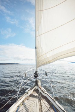 Kayalık göl kıyılarında seyir halindeki ahşap meşe güvertesiyle donatılmış modern bir yat. İskoçya, İngiltere. Güverteden pruvaya, direğe, yelkenlere bakın. Seyahat tutkusu, eğlence aktivitesi, spor, yelkenli yarışı, deniz yolculuğu.