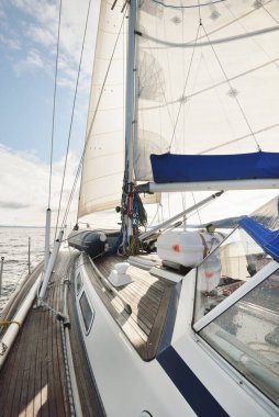 Kayalık göl kıyılarında seyir halindeki ahşap meşe güvertesiyle donatılmış modern bir yat. İskoçya, İngiltere. Güverteden pruvaya, direğe, yelkenlere bakın. Seyahat tutkusu, eğlence aktivitesi, spor, yelkenli yarışı, deniz yolculuğu.