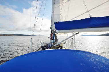 Kayalık göl kıyılarında seyir halindeki ahşap meşe güvertesiyle donatılmış modern bir yat. İskoçya, İngiltere. Güverteden pruvaya, direğe, yelkenlere bakın. Seyahat tutkusu, eğlence aktivitesi, spor, yelkenli yarışı, deniz yolculuğu.