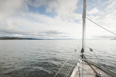 Kayalık göl kıyılarında seyir halindeki ahşap meşe güvertesiyle donatılmış modern bir yat. İskoçya, İngiltere. Güverteden pruvaya, direğe, yelkenlere bakın. Seyahat tutkusu, eğlence aktivitesi, spor, yelkenli yarışı, deniz yolculuğu.