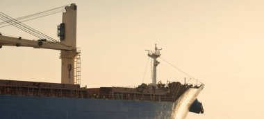 Vinçleri olan büyük bir kargo gemisi gün batımında limandan ayrılıyor. Baltık Denizi. Dramatik fırtına gökyüzü. Yük taşımacılığı, lojistik, küresel iletişim, ekonomi, ticaret, sanayi