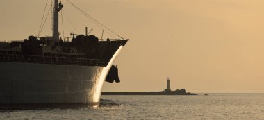 Vinçleri olan büyük bir kargo gemisi gün batımında limandan ayrılıyor. Baltık Denizi. Dramatik fırtına gökyüzü. Yük taşımacılığı, lojistik, küresel iletişim, ekonomi, ticaret, sanayi