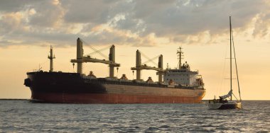 Büyük kargo gemisi (büyük yük gemisi, 179.99 metre uzunluğunda) ve günbatımında Baltık Denizi 'nde yelkenli yelkenli. Yük taşımacılığı, küresel iletişim, ekonomi, seyahat, eğlence. spor