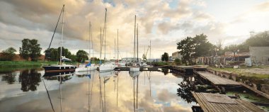 Günbatımında yat limanında demirlemiş zarif ve modern yelkenliler. Dramatik gökyüzü, parlayan altın bulutlar. Tatiller, ulaşım, spor, eğlence, turizm, seyahat, liman