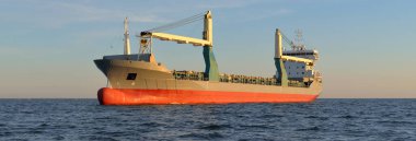 Gün batımında açık denizde yelken açan büyük bir yük vinci gemisi. Altın güneş ışığı. Yük taşımacılığı, deniz taşımacılığı, lojistik, küresel iletişim, ekonomi, iş dünyası, sanayi, dünya çapında nakliye