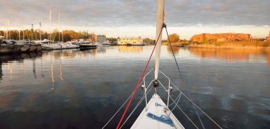 Beyaz yat gün batımında limana varacak. Güverteden pruva ve yelkenlere kadar yakın çekim. Fırtınadan sonra dramatik bir gökyüzü. Baltık Denizi. Deniz aracı, ulaşım, hizmet, spor, eğlence kavramları