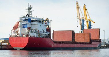Liman terminalinde büyük bir kargo gemisi yükleniyor, arka planda vinçler var. Yük taşımacılığı, lojistik, küresel iletişim, ekonomi, ticaret, sanayi, özel ekipman