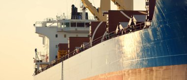 Büyük kargo gemisi (toplu taşıyıcı, 187 metre uzunluğunda) iskele terminalinde yükleme, arka planda vinçler. Yük taşımacılığı, lojistik, küresel iletişim, ekonomi, ticaret, sanayi