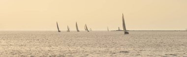 Günbatımında Baltık Denizi 'nde yelken açan topuklu beyaz yelkenli yatlar. Fırtınadan sonra gökyüzü açık, altın güneş ışığı. Ulaşım, seyahat, gezi, spor, eğlence, boş zaman aktivitesi, yarış, yelkenli yarışı