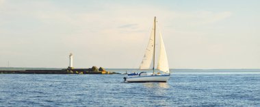Günbatımında Baltık Denizi 'nde yelkenli yelkenli yelkenli. Fırtınadan sonra açık gökyüzü, yumuşak güneş ışığı. Deniz feneri. Ulaşım, seyahat, gezi, spor, eğlence, boş zaman aktivitesi, yarış, yelkenli yarışı