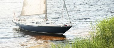 Kumlu kıyıya demirli mavi şalopeli yat (kumsalda otlarla kaplanmış). İsveç 'te, Avrupa' da. Doğa, yaz tatilleri, eğlence, gezi, spor, ulaşım. Hava görünümü