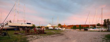 Günbatımında yat limanında duran zarif ve modern yelkenliler. Dramatik gökyüzü, parlayan altın bulutlar. Tatiller, ulaşım, spor, eğlence, turizm, seyahat, liman