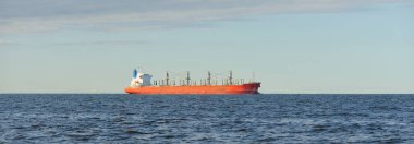 Büyük kırmızı bir yük gemisi (179 metre uzunluğunda) açık bir Baltık Denizi 'nde yüzüyor. Dramatik bir gökyüzü. Yük taşımacılığı, denizcilik gemisi, lojistik, küresel iletişim, ekonomi, iş dünyası, sanayi