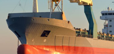 Büyük vinç gemisi (genel yük, 146 metre uzunluğunda) gün batımında açık denizde yol alır. Altın güneş ışığı. Yük taşımacılığı, lojistik, küresel iletişim, ekonomi, sanayi, dünya çapında taşımacılık