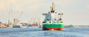 Büyük yeşil yük gemisi gün batımında kargo terminaline varacak. Arka planda gemiler ve vinçler var. Dramatik bulut manzarası. Yük taşımacılığı, küresel iletişim, endüstri, ekonomi, lojistik