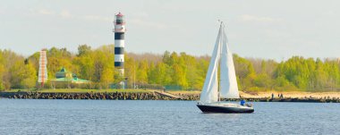 Günbatımında Baltık Denizi 'nde yelkenli yelkenli yelkenli. Fırtınadan sonra açık gökyüzü, yumuşak güneş ışığı. Deniz feneri. Ulaşım, seyahat, gezi, spor, eğlence, boş zaman aktivitesi, yarış, yelkenli yarışı