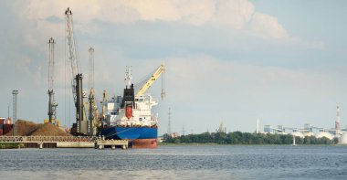 Liman terminalinde büyük bir kargo gemisi yükleniyor, arka planda vinçler var. Yük taşımacılığı, deniz taşımacılığı, lojistik, küresel iletişim, dünya çapında taşımacılık, ekonomi, ticaret, sanayi