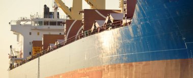 Liman terminalinde büyük bir kargo gemisi yükleniyor, arka planda vinçler var. Yük taşımacılığı, deniz taşımacılığı, lojistik, küresel iletişim, dünya çapında taşımacılık, ekonomi, ticaret, sanayi