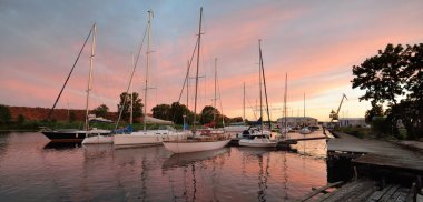 Günbatımında yat limanında demirlemiş zarif ve modern yelkenliler. Dramatik gökyüzü, parlayan altın bulutlar. Tatiller, ulaşım, spor, eğlence, turizm, seyahat, liman