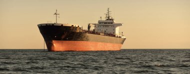 Büyük bir kargo gemisi (kimyasal tanker, 184 metre uzunluğunda) gün batımında açık denizde yol alır. Altın güneş ışığı. Yük taşımacılığı, yakıt, enerji üretimi, denizcilik gemisi, lojistik, ekonomi, sanayi