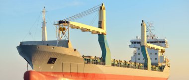 Büyük vinç gemisi (genel yük, 146 metre uzunluğunda) gün batımında açık denizde yol alır. Altın güneş ışığı. Yük taşımacılığı, lojistik, küresel iletişim, ekonomi, sanayi, dünya çapında taşımacılık