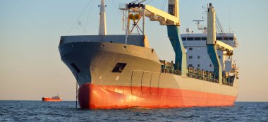 Büyük vinç gemisi (genel yük, 146 metre uzunluğunda) gün batımında açık denizde yol alır. Altın güneş ışığı. Yük taşımacılığı, lojistik, küresel iletişim, ekonomi, sanayi, dünya çapında taşımacılık