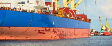 Büyük kargo gemisi (toplu taşıyıcı, 187 metre uzunluğunda) iskele terminalinde yükleme, arka planda vinçler. Yük taşımacılığı, lojistik, küresel iletişim, ekonomi, ticaret, sanayi