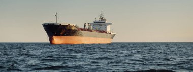 Büyük bir kargo gemisi (kimyasal tanker, 184 metre uzunluğunda) gün batımında açık denizde yol alır. Altın güneş ışığı. Yük taşımacılığı, yakıt, enerji üretimi, denizcilik gemisi, lojistik, ekonomi, sanayi