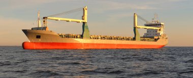 Büyük vinç gemisi (genel yük, 146 metre uzunluğunda) gün batımında açık denizde yol alır. Altın güneş ışığı. Yük taşımacılığı, lojistik, küresel iletişim, ekonomi, sanayi, dünya çapında taşımacılık